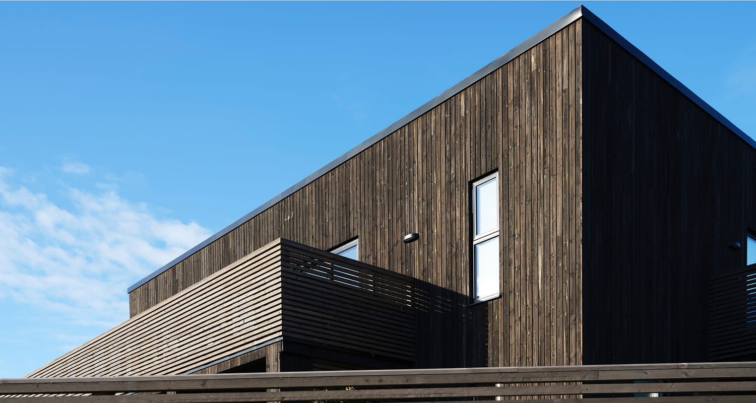 Modernt vinkelhus i mörkt trä med öppen balkong mot klarblå himmel