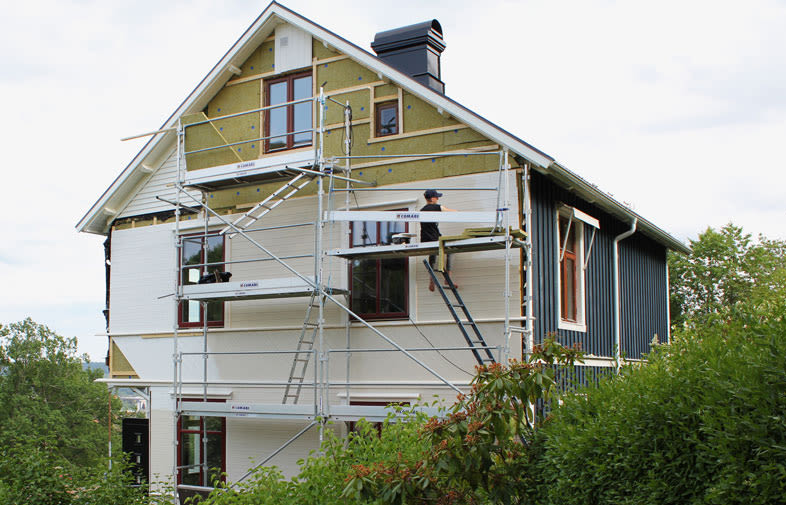 Vitt och mörkblått hus under renovering med ställning, byggarbetare och grön omgivning