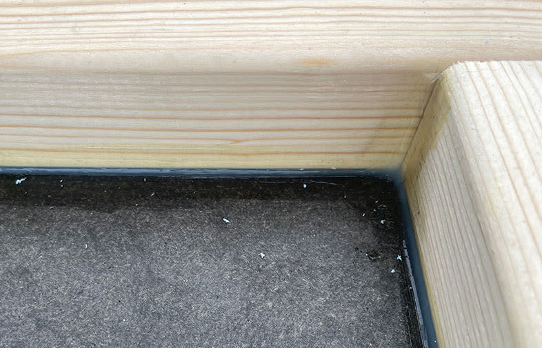 Närbild av ljus furuhörn med svart tätningsfog mot mörkgrå matta