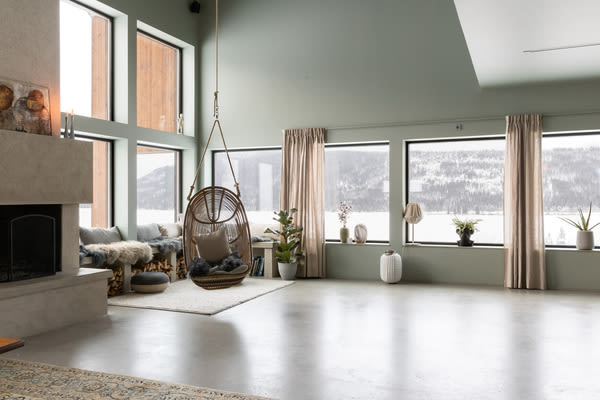 Ljust vardagsrum med mintgröna väggar, stora fönster mot snötäckt vy och hängande rottingfåtölj.