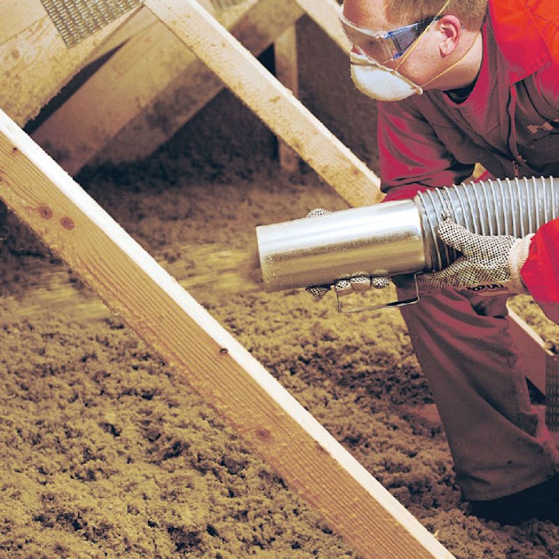 Hantverkare med rör blåser grå isoleringsull mellan träreglar i takkonstruktion