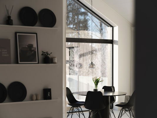Ljus matsal med svart runt bord, stolar, hylla med svarta tallrikar, vas med tulpaner, fönster mot snöig skog