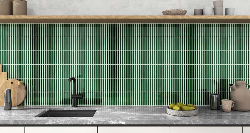 Modern köksbänk med grön mosaik, svart kran, marmorbänk, skärbrädor och fat med päron.