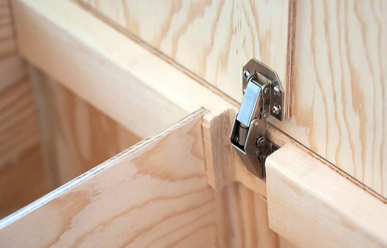 Närbild av ljus träskåpsdörr och silverfärgat metallgångjärn.