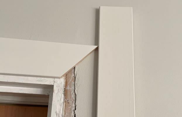 Vit dörrkarm under renovering mot ljusgrå vägg, rå trä- och gipsskikt synligt.