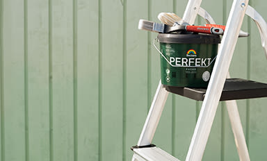 Vit stege med grön "Perfekt"-färgburk och penslar framför ljusgrön panelvägg.