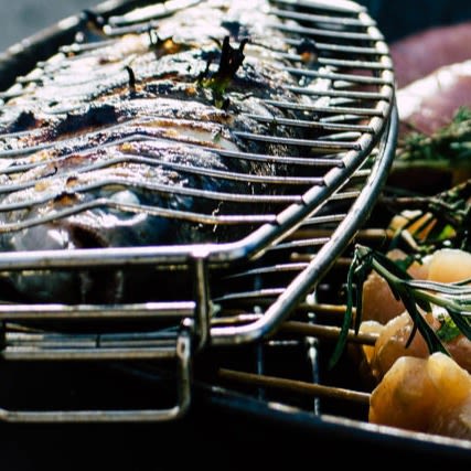 Silvrig grillad fisk i rostfritt galler med gula potatisar och gröna örtkvistar
