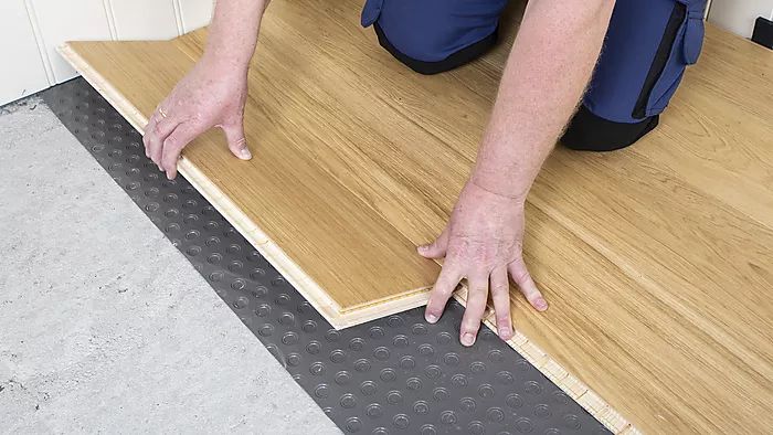 Händer som lägger ljus träplanka på svart bubbelmatta över grå betong.