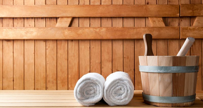 Två vita handdukar på bastubänk, trävägg i bakgrunden och träkare med skopa.