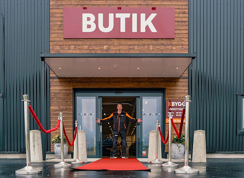 En butikentré med röd matta och avspärrningsrep, där en person står i dörröppningen och välkomnar besökare.