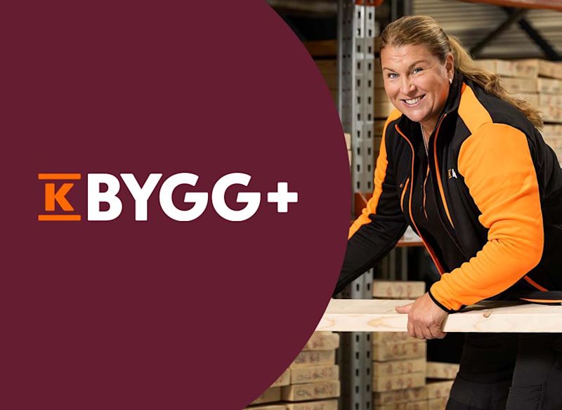 En person i svart och orange arbetskläder håller i en träregel i ett lager med staplade byggmaterial, bredvid en vinröd yta med texten "K BYGG+".