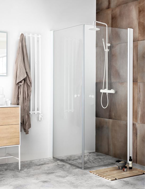 Ljust badrum med glasdusch, brun kakelvägg, vit handdukstork med hängande badrock och träkommod.