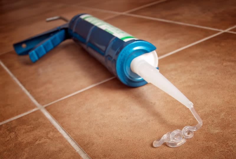 Blå fogspruta på brunt kakelgolv pressar ut genomskinlig tätningsmassa.