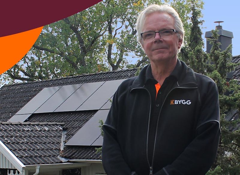 Man i K Bygg-jacka framför villa med solpaneler och grönskande träd.