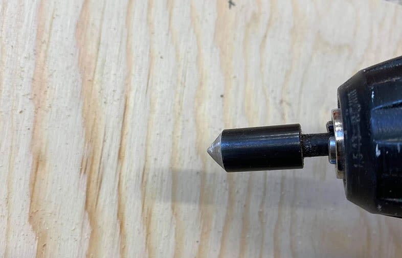 Svart borrbit med silverfärgad spets i borrchuck på ljus träyta