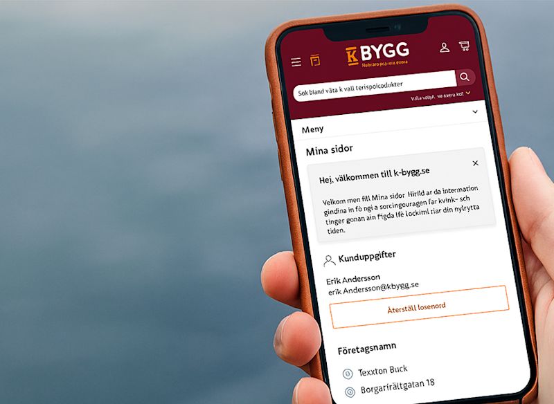 En person håller en mobiltelefon som visar K-Byggs "Mina sidor", där användaren kan se konto- och företagsuppgifter samt hantera sitt konto direkt i mobilen.
