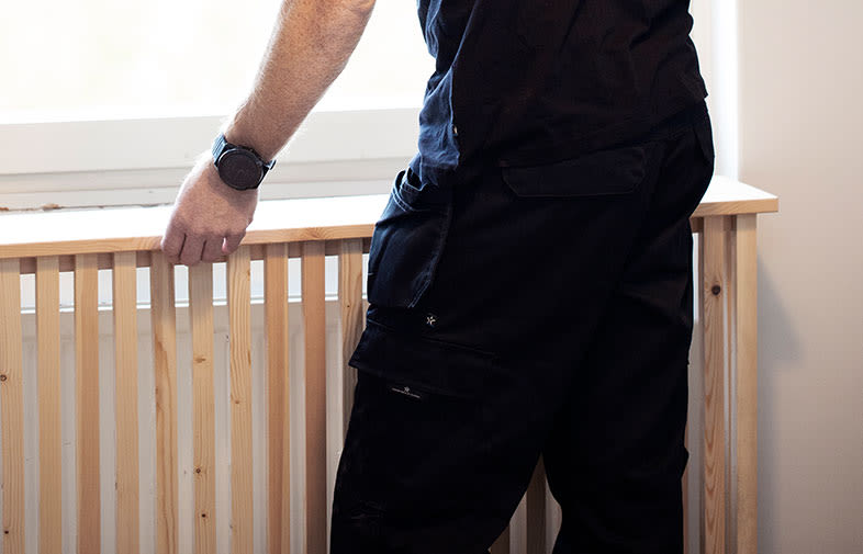 Närbild på person i svarta arbetskläder som monterar ljus träpanel framför fönster.