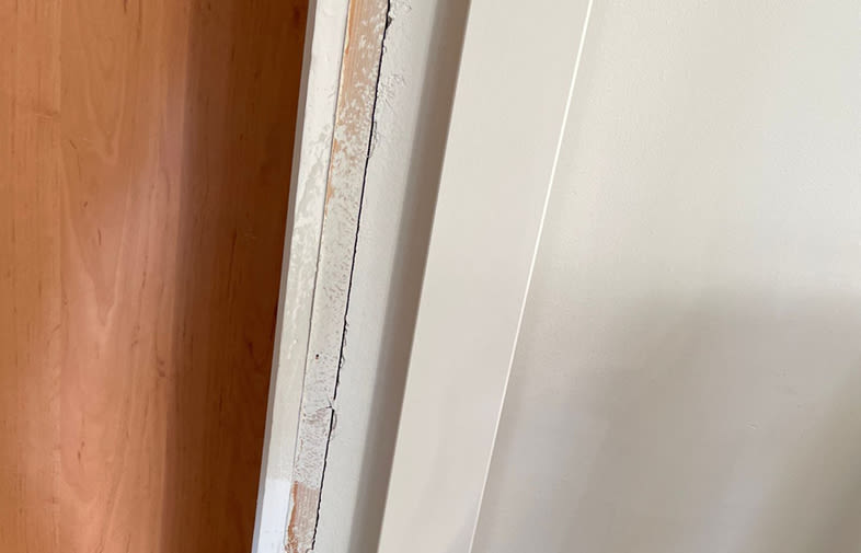 Detaljbild av en sliten vit dörrkarm med flagnande färg intill en orange träddörr.