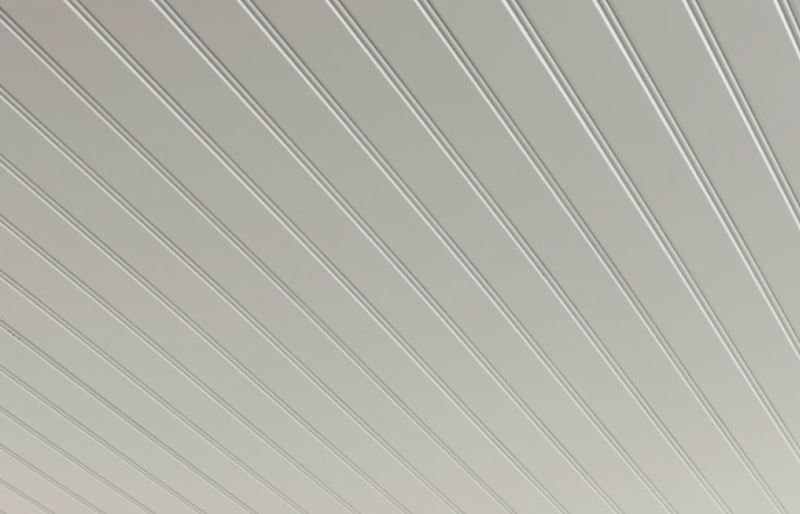 Ljusgrå-beige takpanel med tunna parallella ränder i perspektiv.