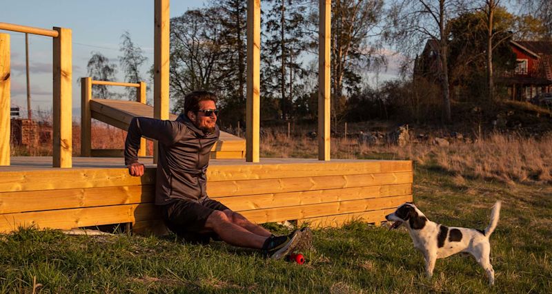 Man i svart träningskläder gör dips vid träplattform i gyllene kvällsljus, vitsvart hund bredvid