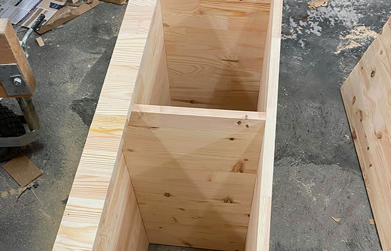 Oljad furulåda med två fack i snickarverkstad, sågspån på betonggolv.