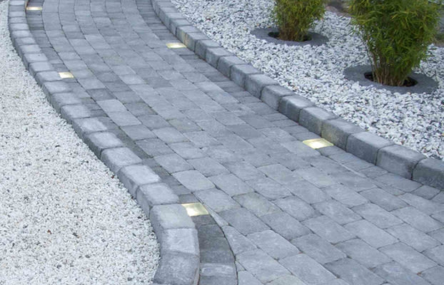 Grå, kurvad stenbelagd gång med infällda ljus, vitt grus och bambu.