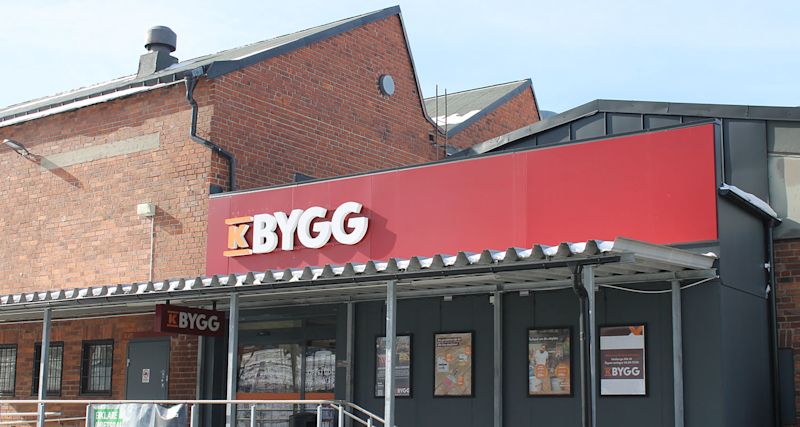 Ingång till K-Bygg-butik med röd fasadskylt på tegelbyggnad och snötäckt plåttak