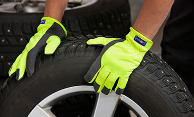 Mekanikers händer i neongula skyddshandskar håller ett bildäck vid bilservice.