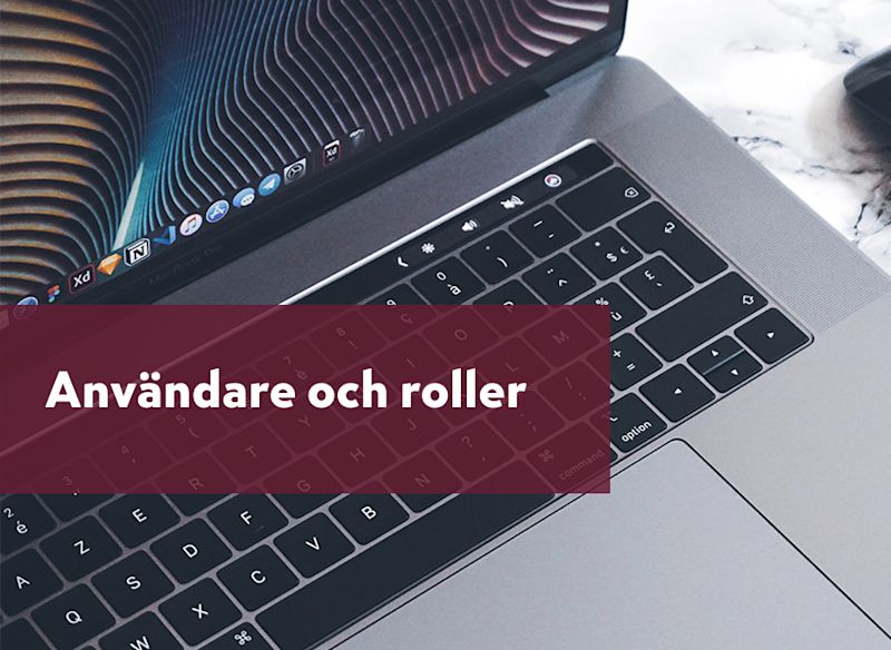 närbild på en öppen laptop i metall, med fokus på tangentbordet och nedre delen av skärmen. Ovanpå ligger en vinröd transparent ruta med texten “Användare och roller”.
