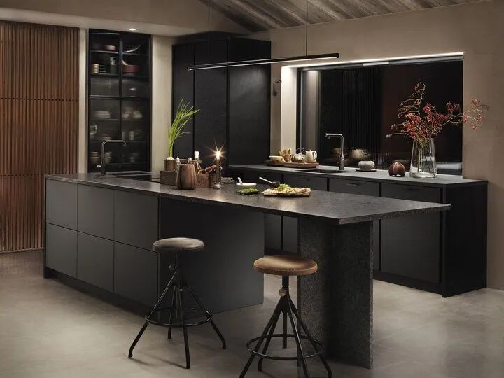 Mörk, modern köksö i antracit med svarta skåp, barstolar, avlånga lampor och växter