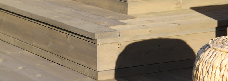 Ljust trädäck med inbyggd sittbänk i trä, skugga och rottingkorg vid kanten