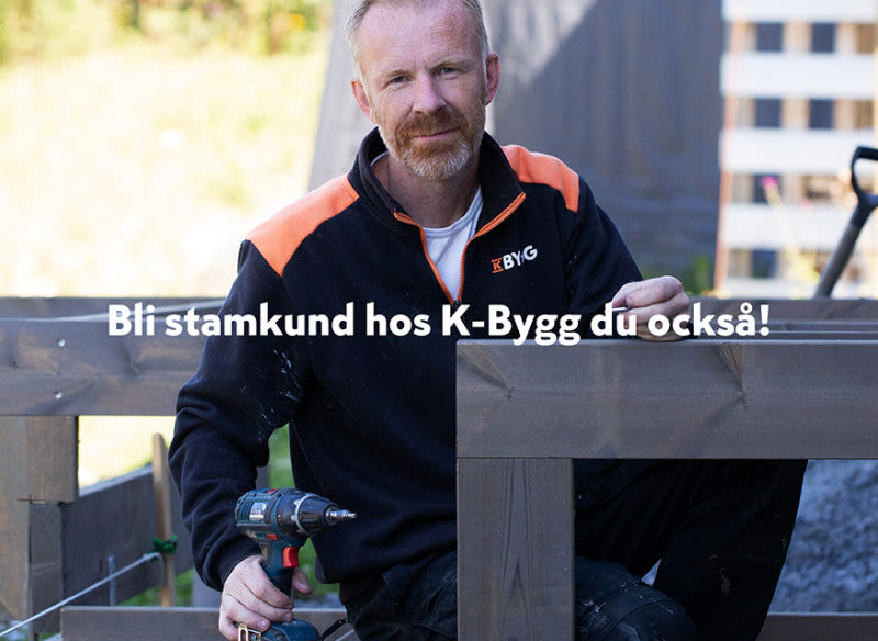 Hantverkare i svart-orange jacka med borrmaskin monterar brunt trästaket utomhus.