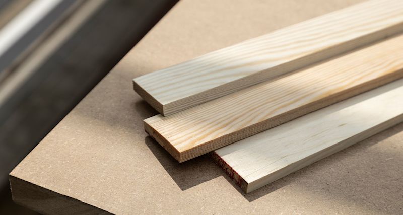 Tre ljusa träplankor med synliga årsringar på beige bordsskiva i solljus.