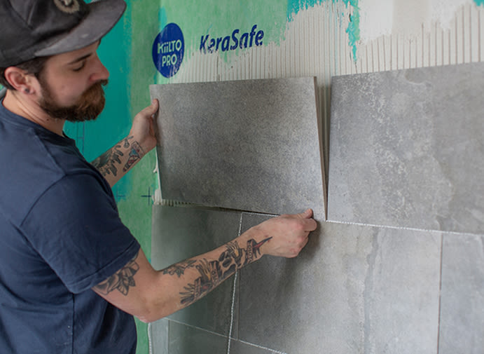 Tatuerade armar sätter stora grå plattor på grön Kiilto Pro KeraSafe-membran.