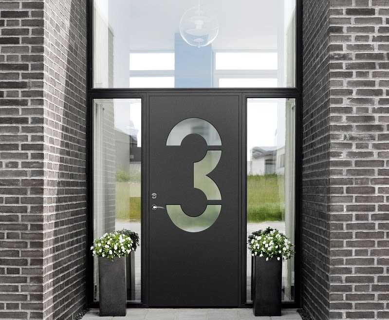 Svart ytterdörr med frostat glas i form av siffran 3 i tegelportal, vita blommor i svarta krukor