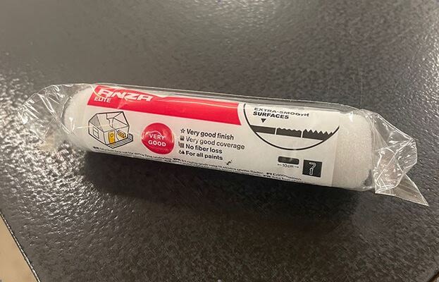 Vit skumfärgrulle i genomskinlig plastförpackning med röd ’Enza Elite’-etikett på svart bänk.