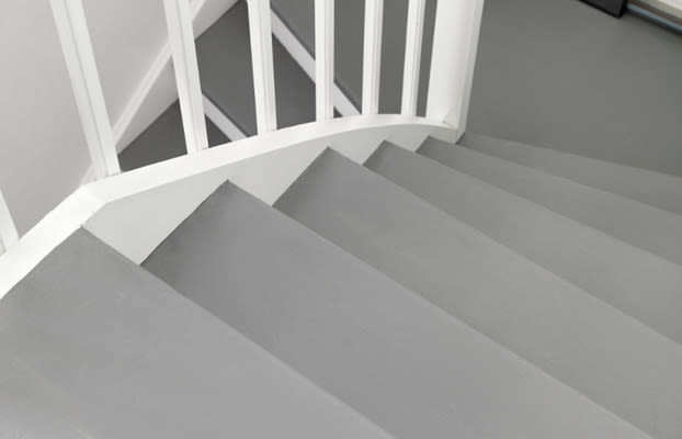 Vy uppifrån av grå trappa med vit spjälräcke mot vit vägg