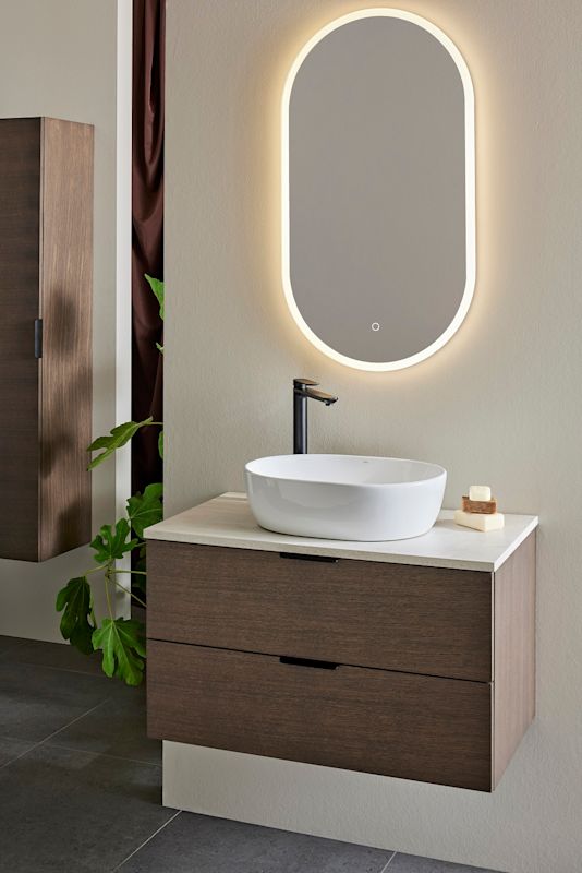 Modern badrumskommod i mörkt trä med vit ovalt handfat, svart kran och belyst spegel
