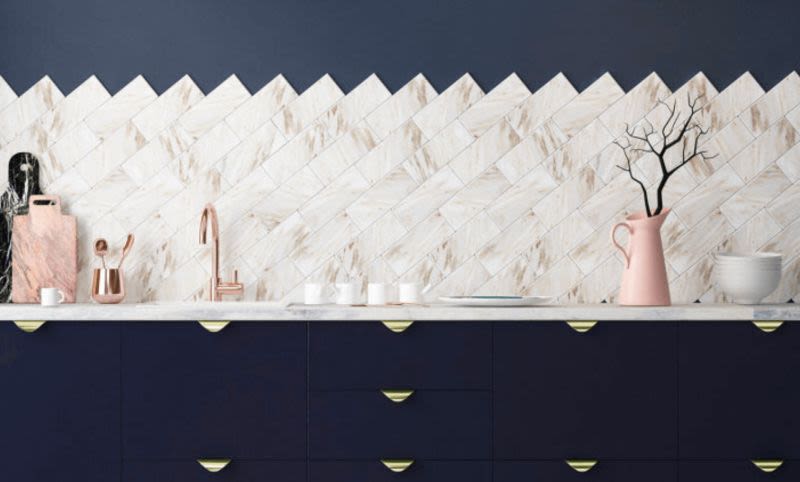 Modern köksbänk med marinblå luckor, vit marmorbacksplash, roséguldkran, rosa vas med grenar