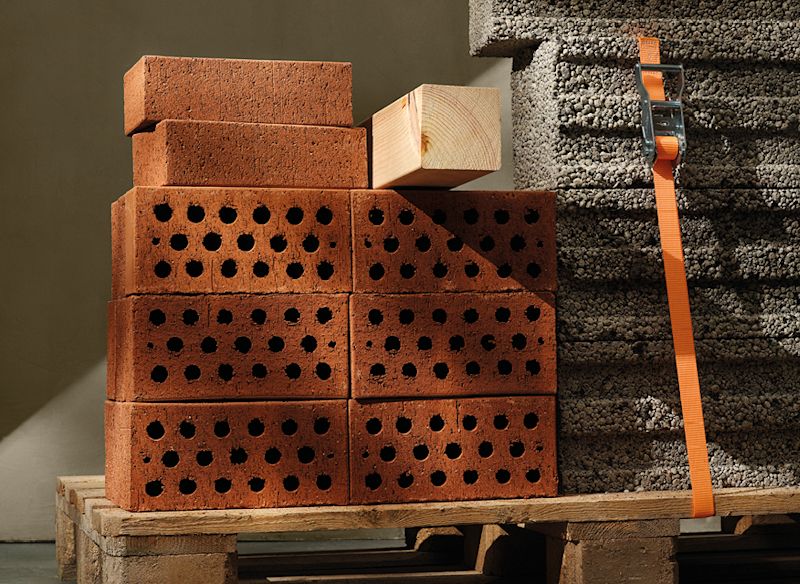 Röda håltegel på träpall bredvid grå isoleringsblock fastspända med orange band