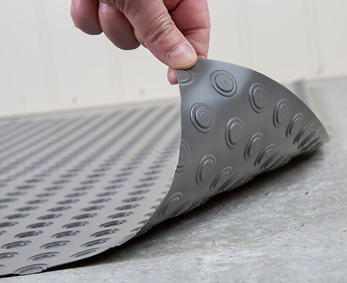 Hand lyfter hörn av grå halkskyddsmatta med cirkulära sugkoppar mot ljust golv.