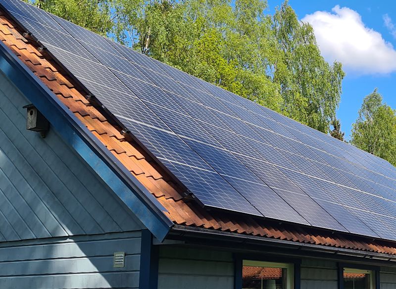 Ljusblått hus med solpaneler på taket, blå himmel och vita moln.