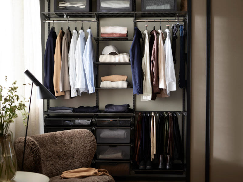 Öppet svart ställ med blazers, skjortor, tröjor, hatt, skärp och stövlar bredvid fåtölj