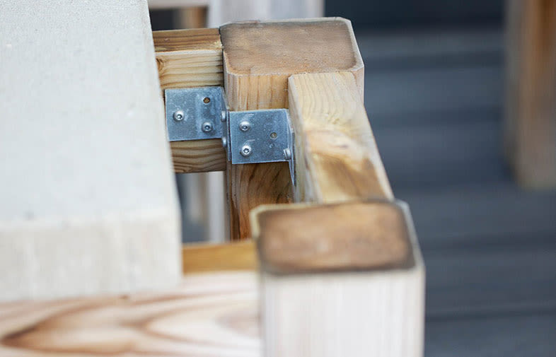 Detalj av ljus furubjälke med galvaniserat vinkelbeslag under vit skiva.