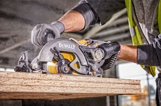 Närbild på snickare i gul varselväst som sågar spånskiva med grå-gul DeWalt cirkelsåg.