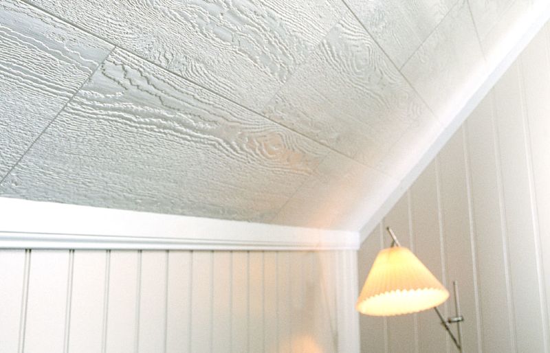 Snedtak i vitt trä med tydlig ådring, beige väggpanel och varm gul golvlampa.