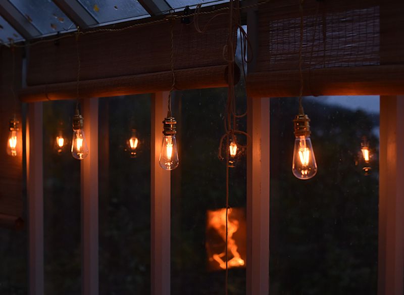 Fem varmgula glödlampor hänger framför mörkt glasfönster med bamburullgardin.