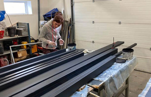 Person i verkstad målar svarta träreglar på plastad arbetsbänk framför vit garageport.
