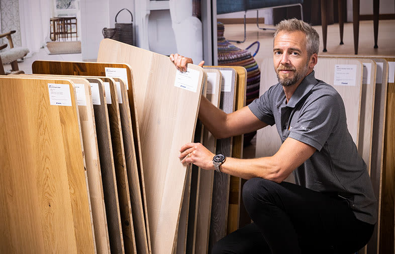 Person i grå pikétröja väljer ljusa och mörka golvprover i trä i butiksmiljö