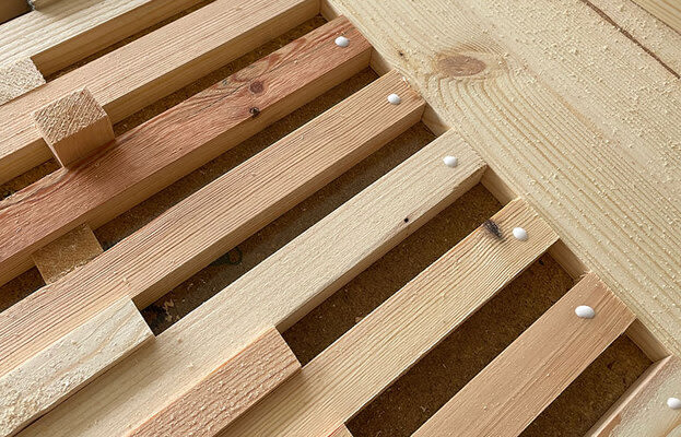 Närbild på parallella ljusa träslatsar med vita limdroppar och sågspån i hörnet.